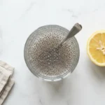 Ein Glas Kaulquappen-Wasser mit gequollenen Chiasamen und Zitrone auf weißem Marmor