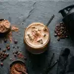 Fertiger ESN Flexpresso Proteinkaffee im Glas mit Kaffeebohnen und Messlöffel auf dunklem Untergrund