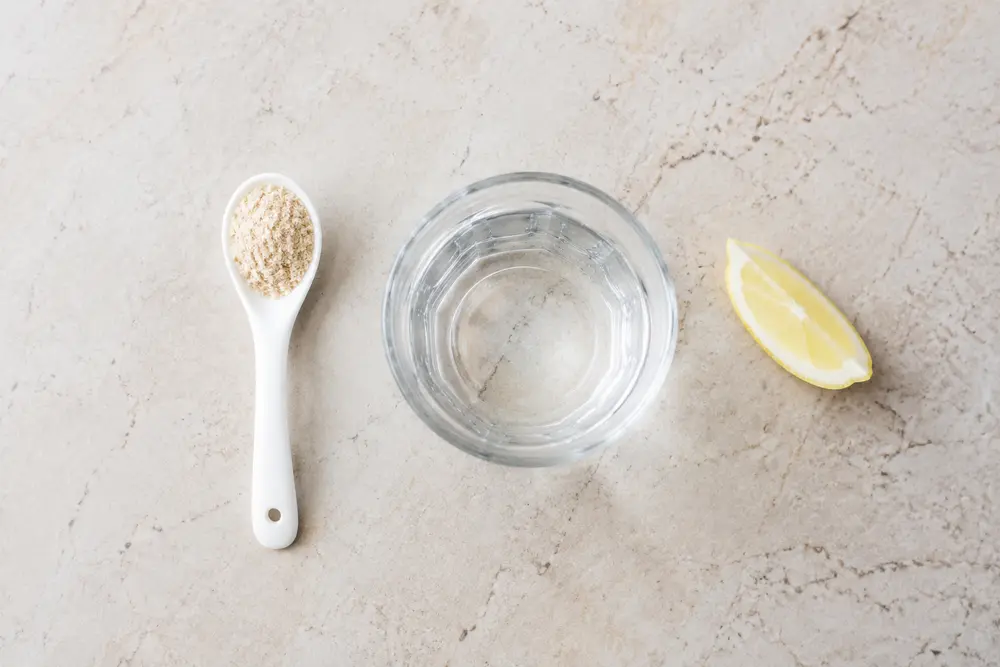 Ein Teelöffel Flohsamenschalen, ein Glas Wasser und eine optionale Zitronenspalte